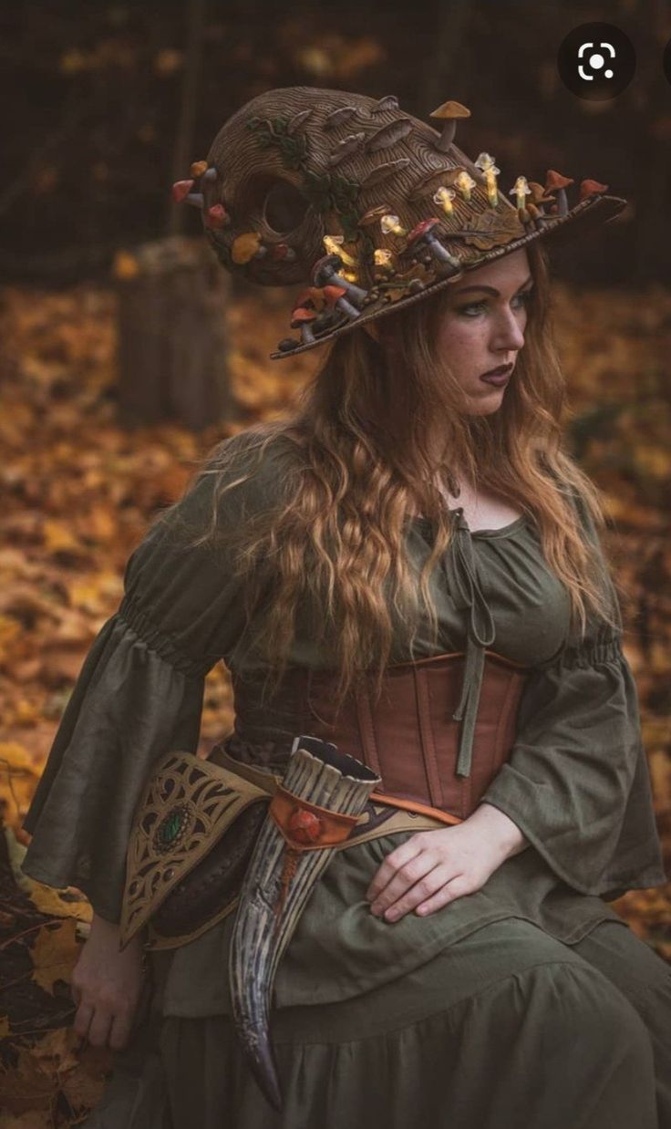 a woman wearing a green dress and hat sitting in the woods with leaves on her head