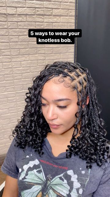 a woman with long curly hair sitting in front of a brick wall and looking down at her phone