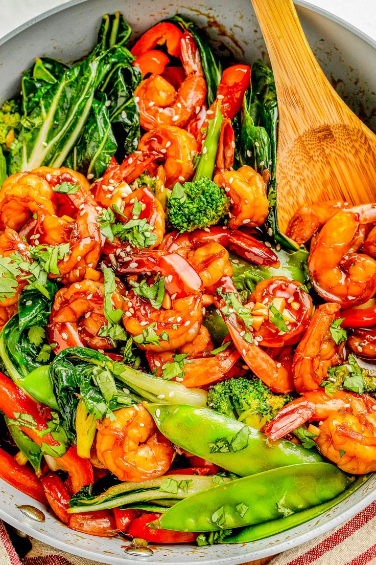 shrimp and broccoli stir fry in a pan with a wooden spoon