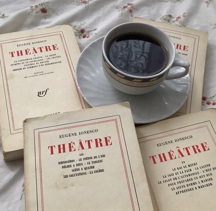 three old books and a cup of coffee on a white tablecloth with floral designs