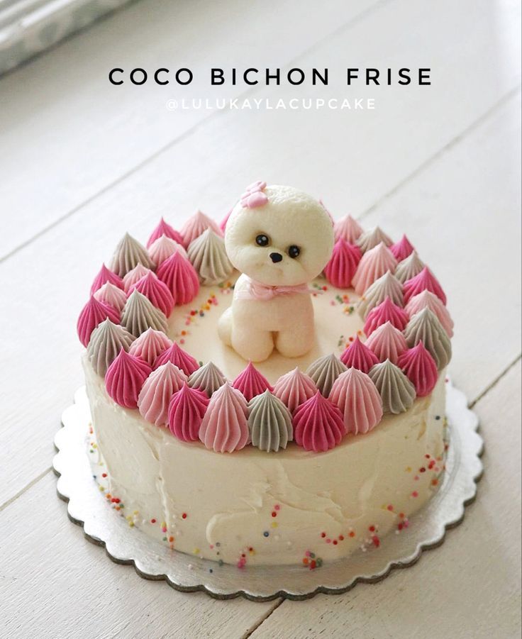 a white cake with pink frosting and a small teddy bear on top that is sitting in the middle of it