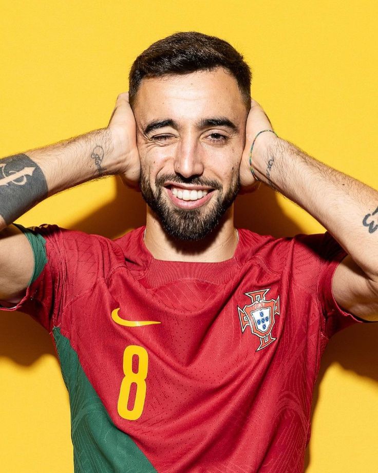 a man with tattoos on his arms and face, wearing a portugal shirt in front of a yellow background