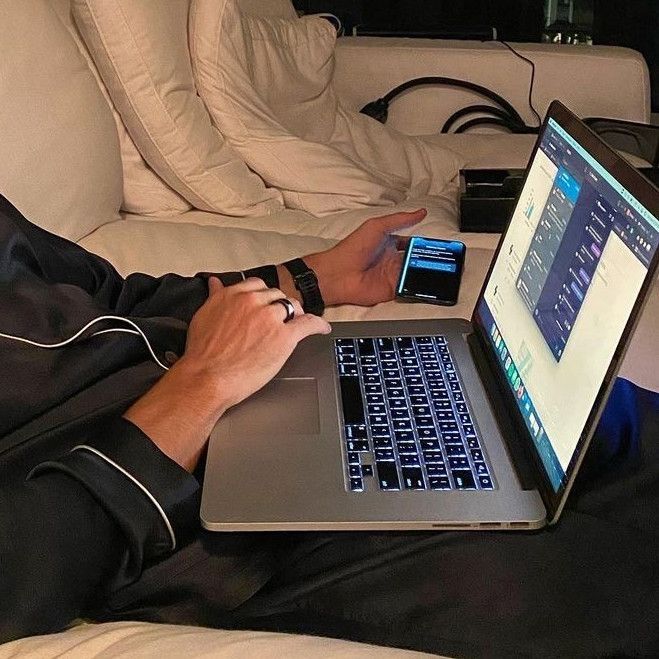 a person sitting on a couch using a laptop computer with their cell phone in front of them