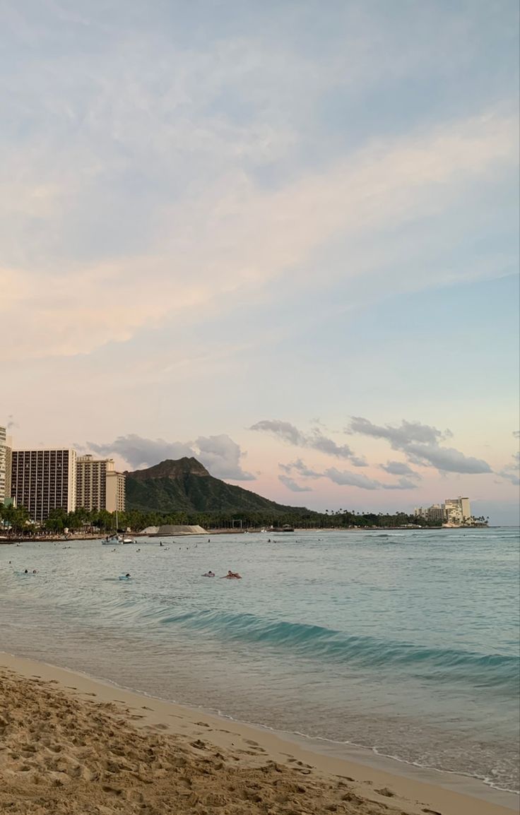 a beach with buildings in the background and people swimming in the water at sunset or sunrise