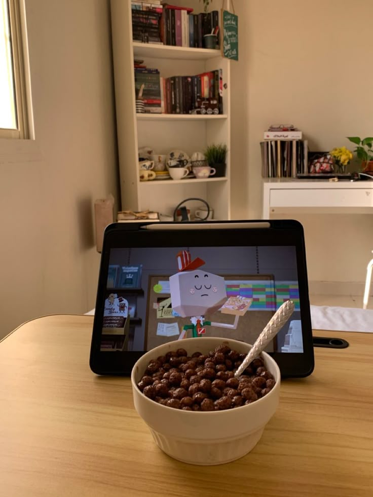 a bowl of cereal sitting on top of a table next to an open laptop computer