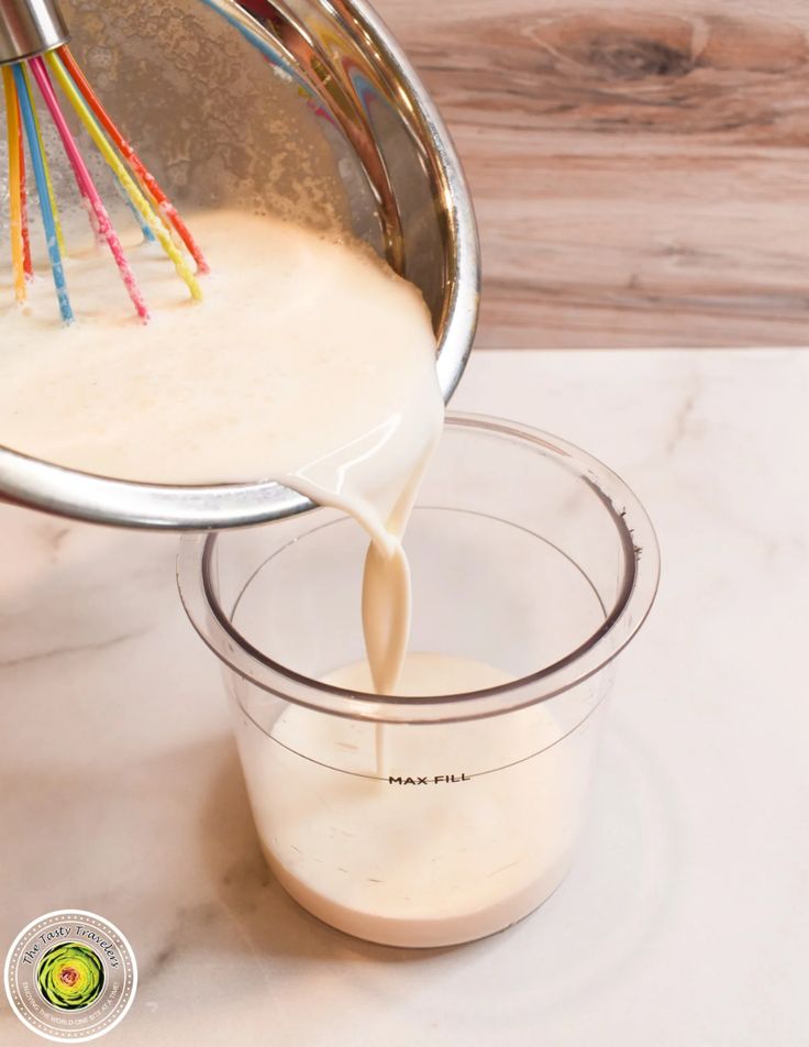 a person pouring milk into a glass bowl