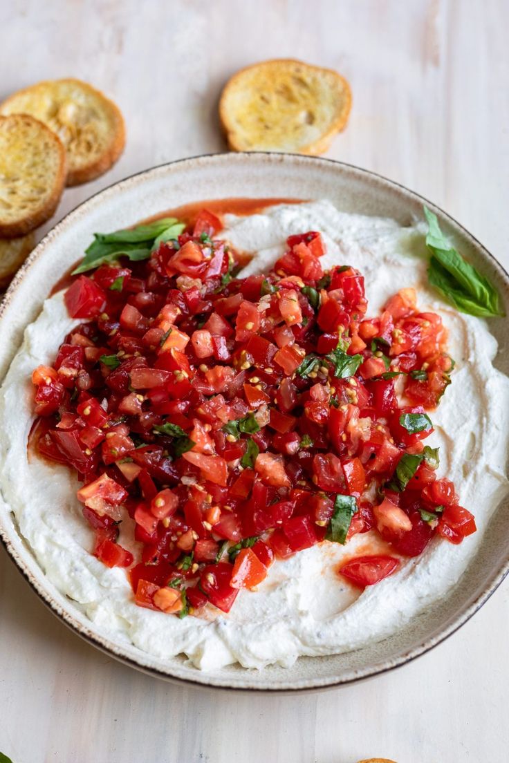 a bowl filled with mashed potatoes and garnished with tomato relish next to slices of bread