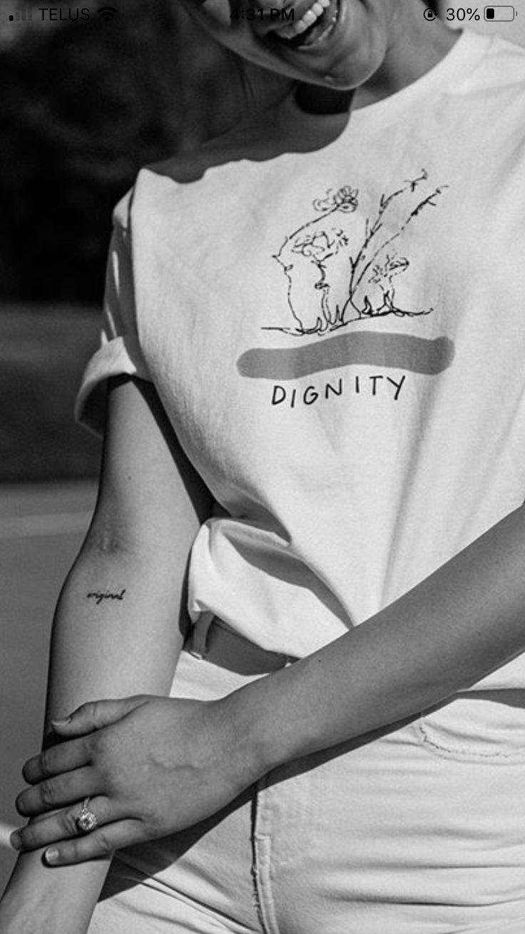 black and white photograph of a woman smiling with her hands on her hips, wearing a t - shirt that says dignify