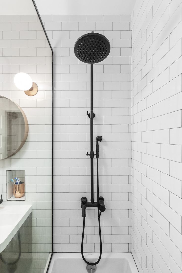 the shower head is connected to the faucet in this white tiled bathroom with black fixtures