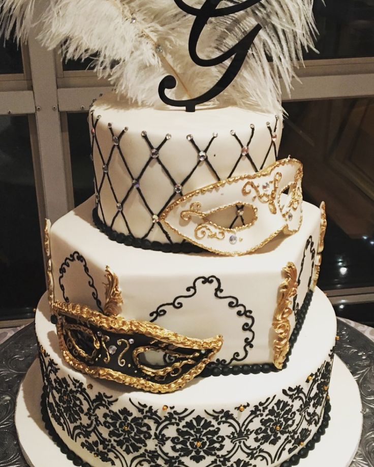 a three tiered cake decorated with black and white designs, gold accents and feathers