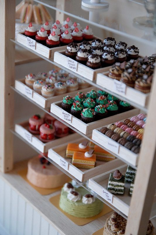 a display case filled with lots of different types of cupcakes on top of wooden shelves