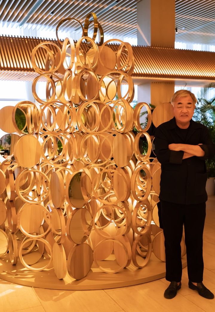 a man standing in front of a sculpture made out of wooden circles and circular rings