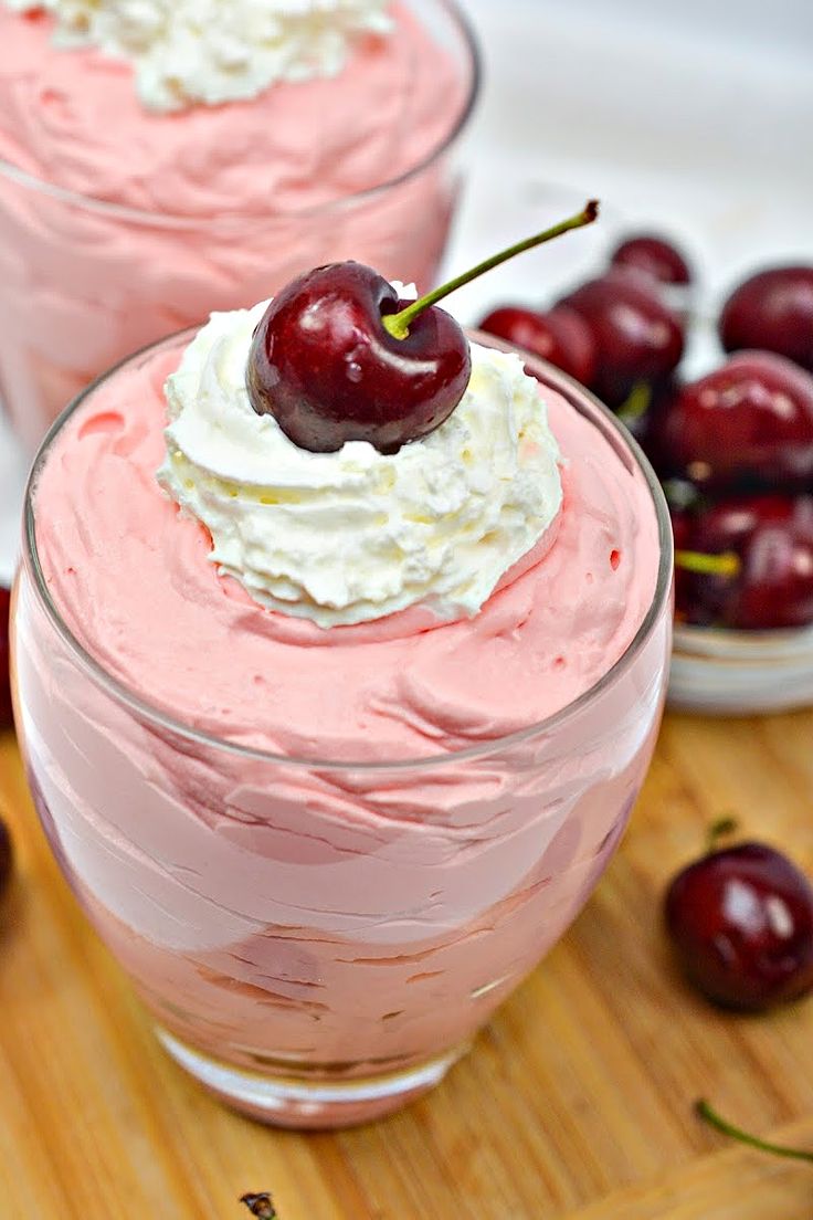 two desserts with cherries and whipped cream in them on a cutting board next to bowls of cherries