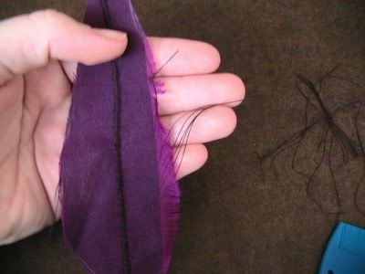 a person is holding a purple feather in their left hand and the other hand has a blue piece of cloth on it