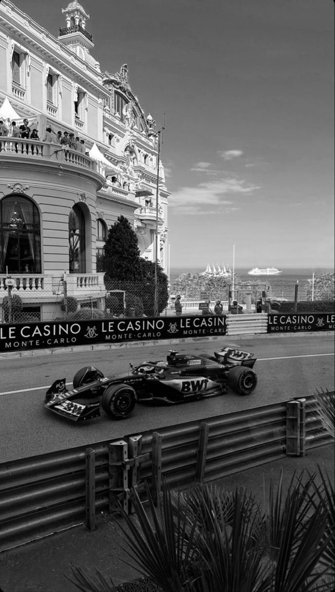 black and white photograph of two racing cars in front of a building