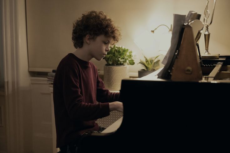 a young boy sitting at a piano in front of a light that is turned on