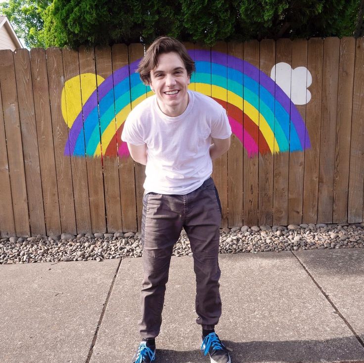 a young man standing in front of a wooden fence with a rainbow painted on it