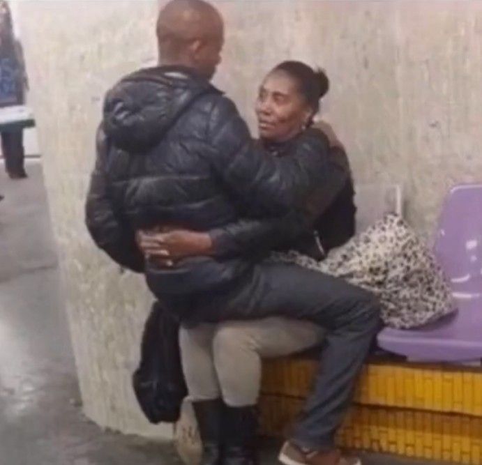 a man and woman sitting on a bench in front of a wall with purple chairs