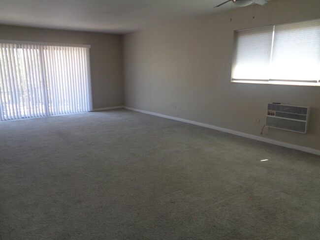 an empty living room with large windows and blinds on the sliding glass doors that lead out to outside