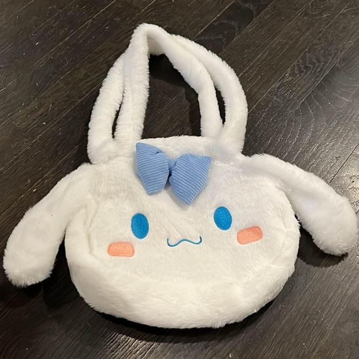 a stuffed animal purse with a blue bow on it's head sitting on a wooden floor