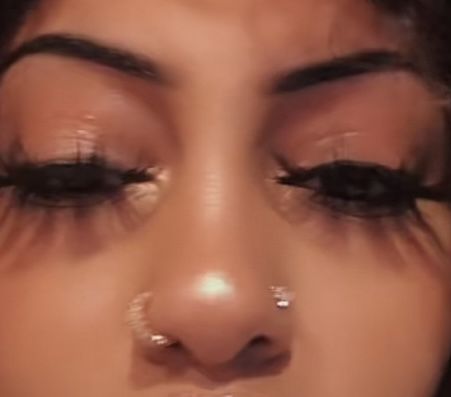 a close up of a woman's face with fake eyelashes and piercings on her nose