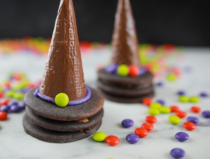 two chocolate cones with candy on top and one has a witches hat on it, surrounded by colorful candies