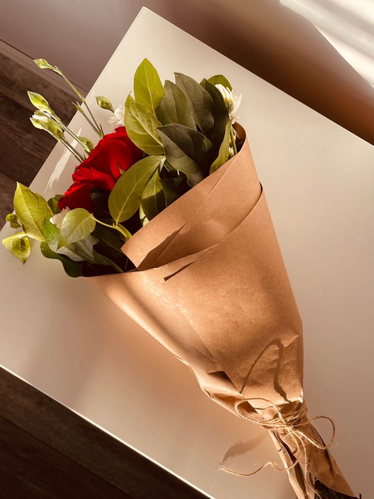 a bouquet of red roses wrapped in brown paper on a white counter top with wood flooring