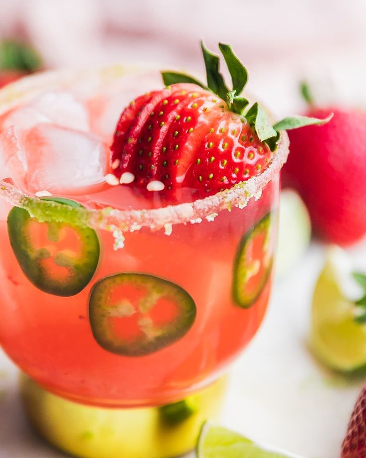 a strawberry and cucumber cocktail garnished with limes on the rim