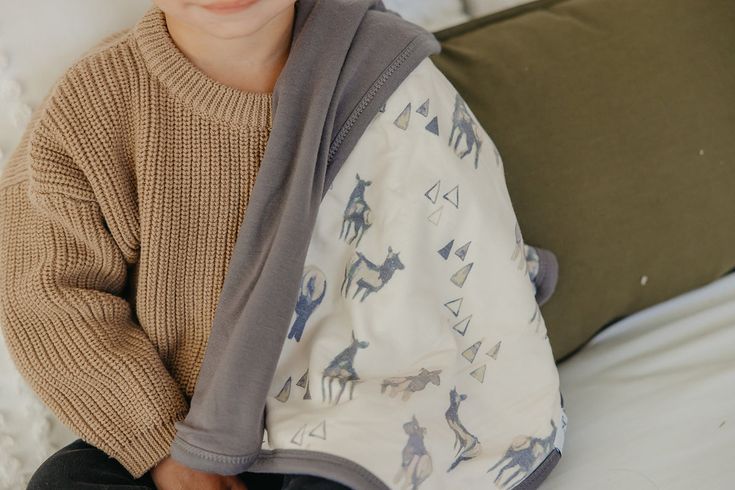 a young boy sitting on top of a bed wearing a sweater and smiling at the camera