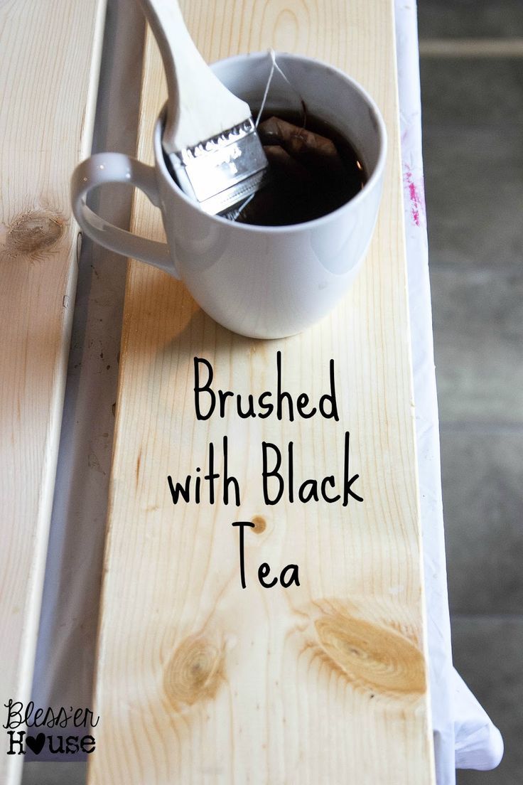 a wooden table topped with a white cup filled with black tea next to a spoon