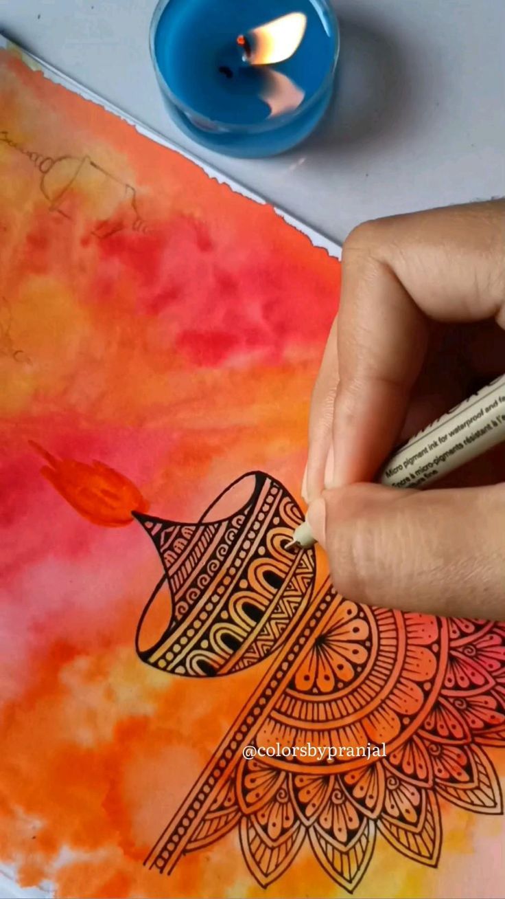 a person is drawing on a piece of paper with watercolors and a blue candle in the background