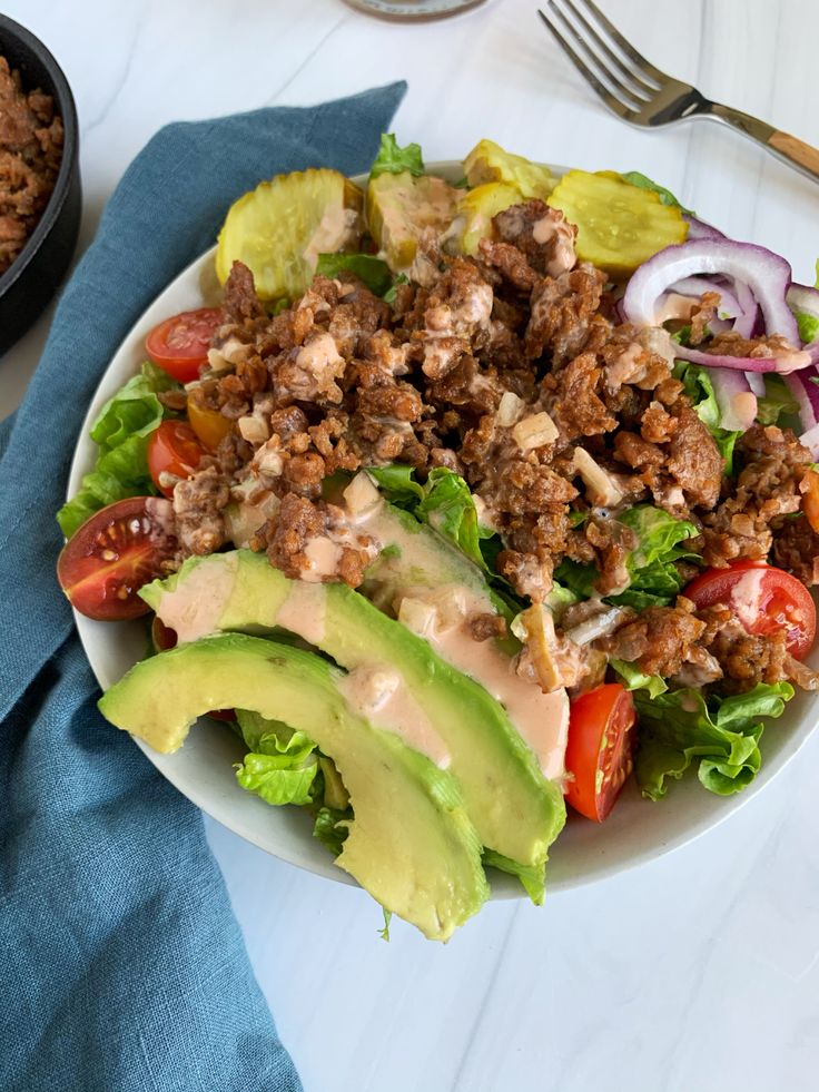 a salad with meat, tomatoes, lettuce and onions on a white plate