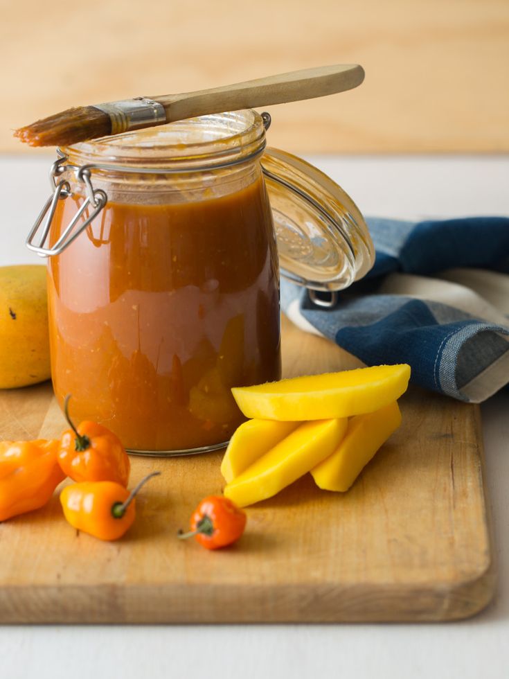 a wooden cutting board topped with a jar of peanut butter next to bananas and peppers