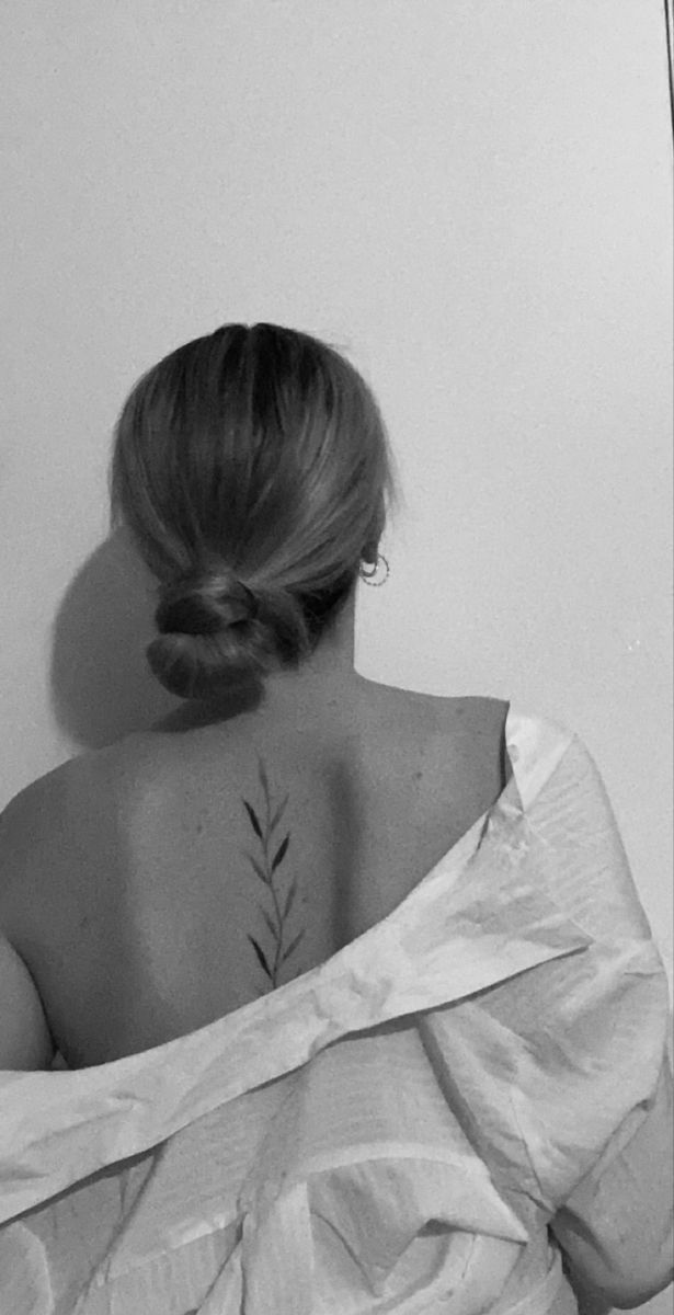 the back of a woman's neck with a small plant tattoo on her left shoulder