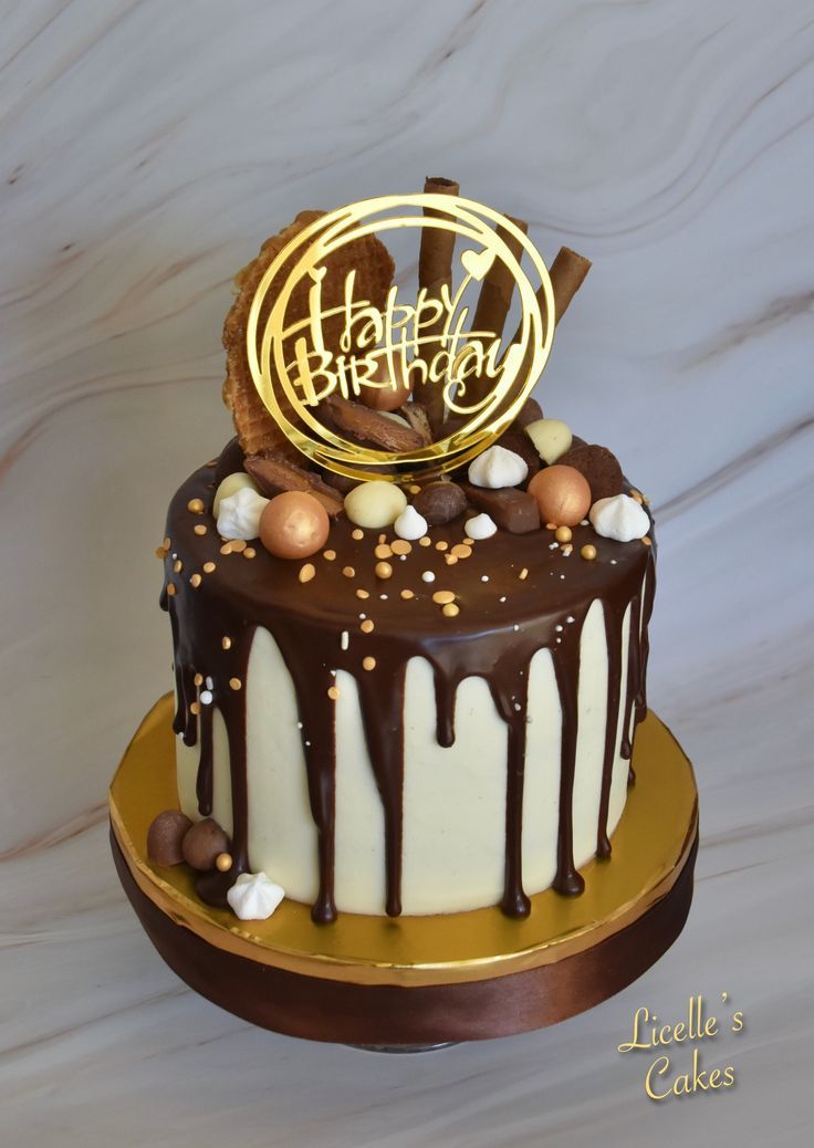 a birthday cake with chocolate icing and nuts on top that says happy birthday written in gold