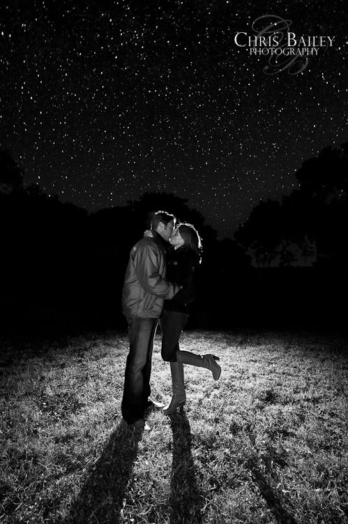 a man and woman kissing in the middle of a field at night with stars above them