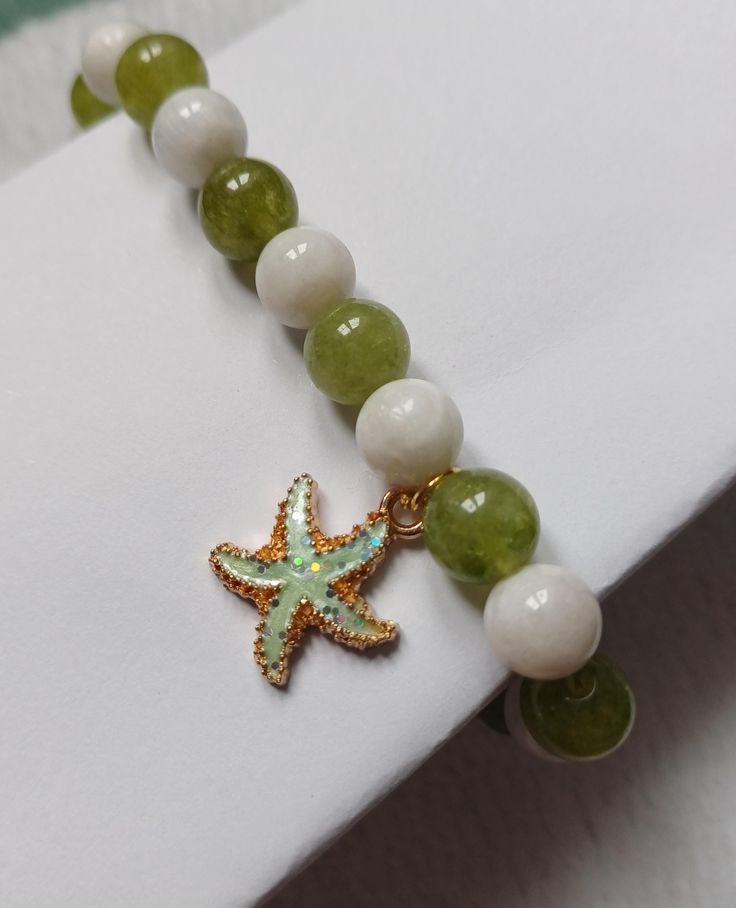 Fit wrist 8" down Lovely round beads in green and white Gorgeous enamel coated starfish charm, all on a strong elastic White Star-shaped Jewelry With Starfish Charm, White Star-shaped Ocean-inspired Jewelry, Ocean-inspired White Star-shaped Jewelry, Ocean-inspired White Star Jewelry, Adjustable Green Starfish Jewelry, White Starfish Charm Bracelet, Green Starfish Charm Jewelry As Gift, Adjustable White Jewelry With Starfish Charm, White Charm Bracelet With Star Charm As Gift