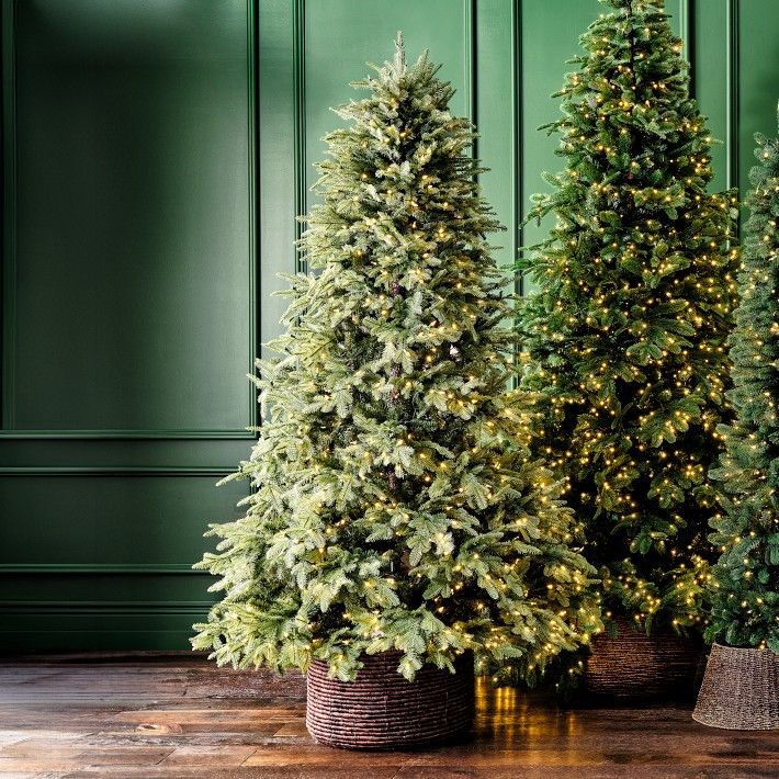 three artificial christmas trees in baskets on the floor next to green walls and wooden floors