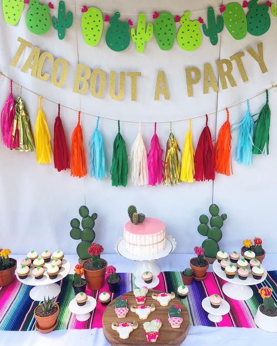 a table topped with cupcakes and tacos next to a banner that says taco bout a party