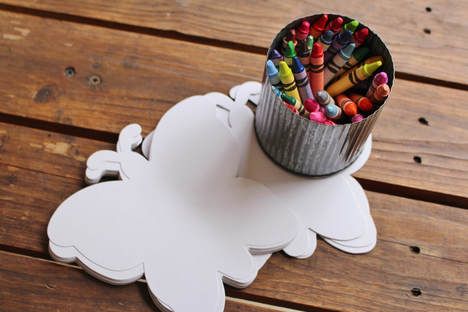 a cup filled with crayons sitting on top of a wooden table next to a tin