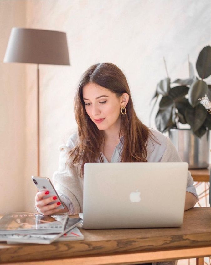 a woman sitting at a table with a laptop and cell phone