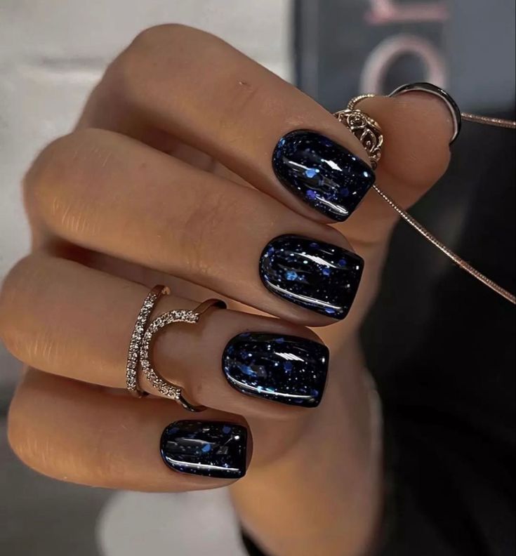 a woman's hand with blue and black nail polishes on it, holding two rings