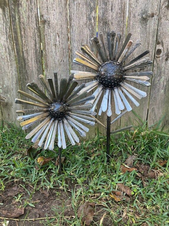 two metal sunflowers sitting on top of green grass next to a wooden fence