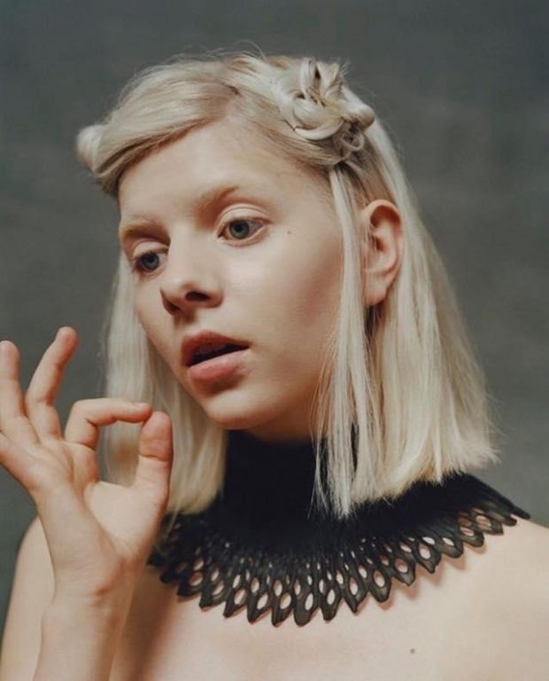 a woman with blonde hair wearing a black top and holding her hand up to her face