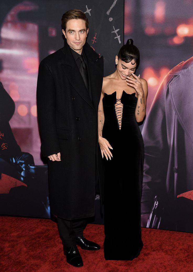 a man and woman standing next to each other in front of a batman movie poster