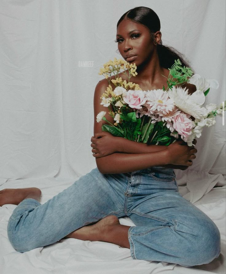 a woman sitting on the floor with flowers in her lap and arms around her body