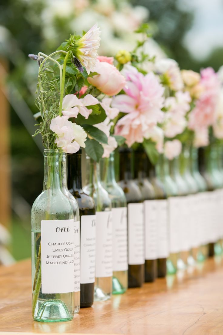 several bottles with flowers in them are lined up on a wooden table, along with labels for each bottle