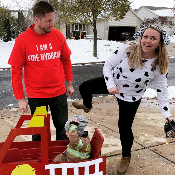 a man and woman standing next to a child in a toy firetruck