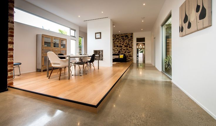 a large open living room and dining area with wood flooring, white walls and windows