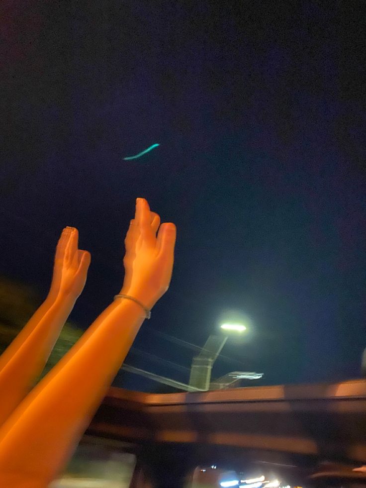 someone is flying a kite in the dark sky at night with their hands raised up